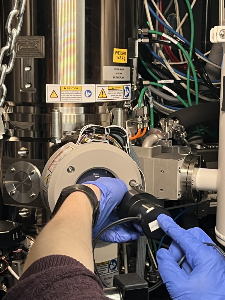 Des mains insèrent l'échantillon dans le porte échantillon du microscope électronique en transmission